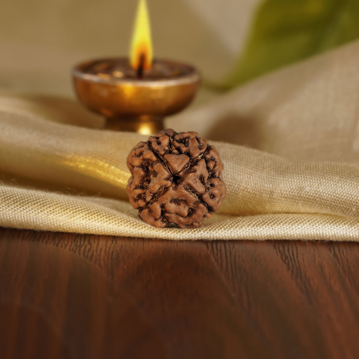 Front of the 4 Mukhi Rudraksha on silk beside a brass diya